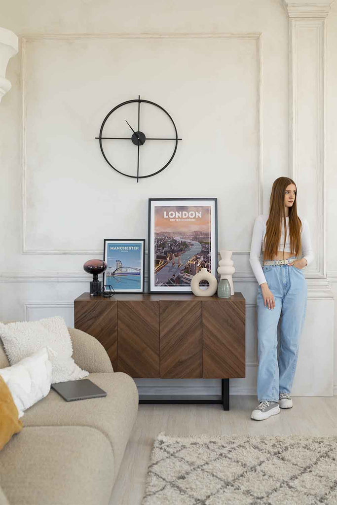 Woman standing in a living room with a wooden sideboard, sofa, and wall decor.